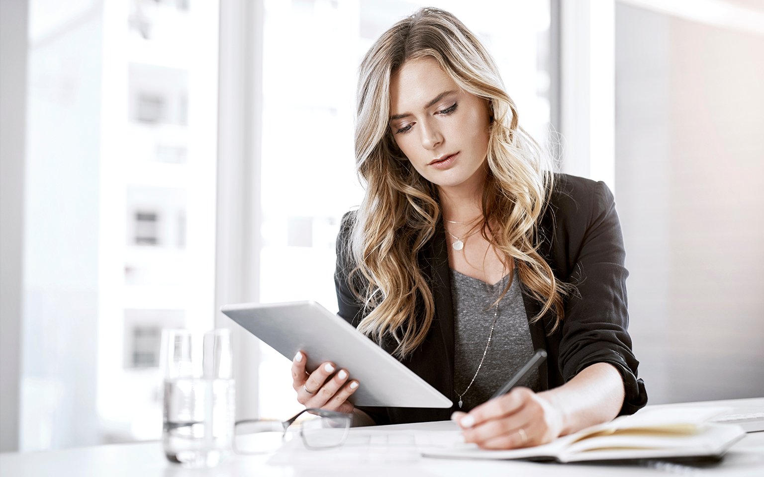 woman writing while looking at the tablet